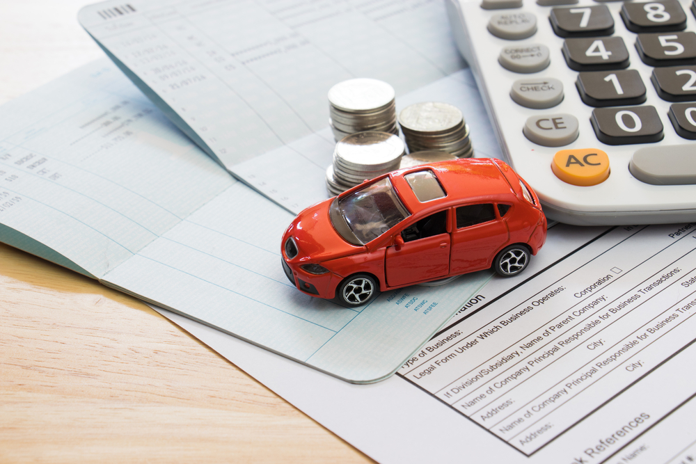 A mini car model representing the finance process with pinched pennies and a payment calculator along with the paperwork where you can get the best deal in Akron, OH 